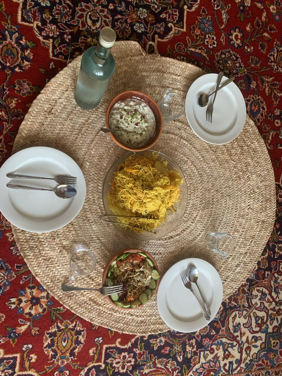 A sofreh laid out on a Persian rug, with rice, stew, salad and bread shared from the floor.