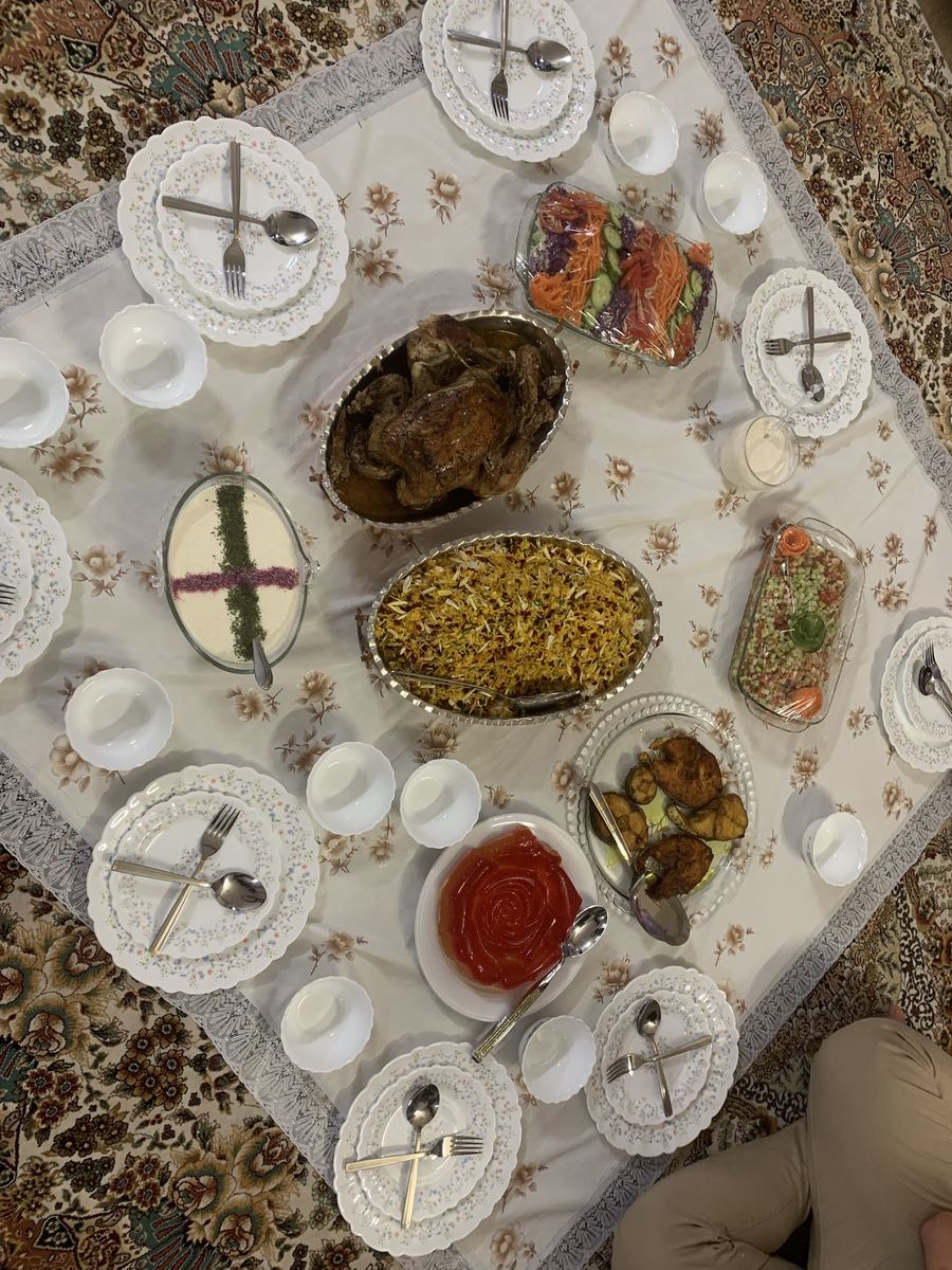 A family sofreh spread across a tablecloth with roast chicken, jewelled rice and salads.