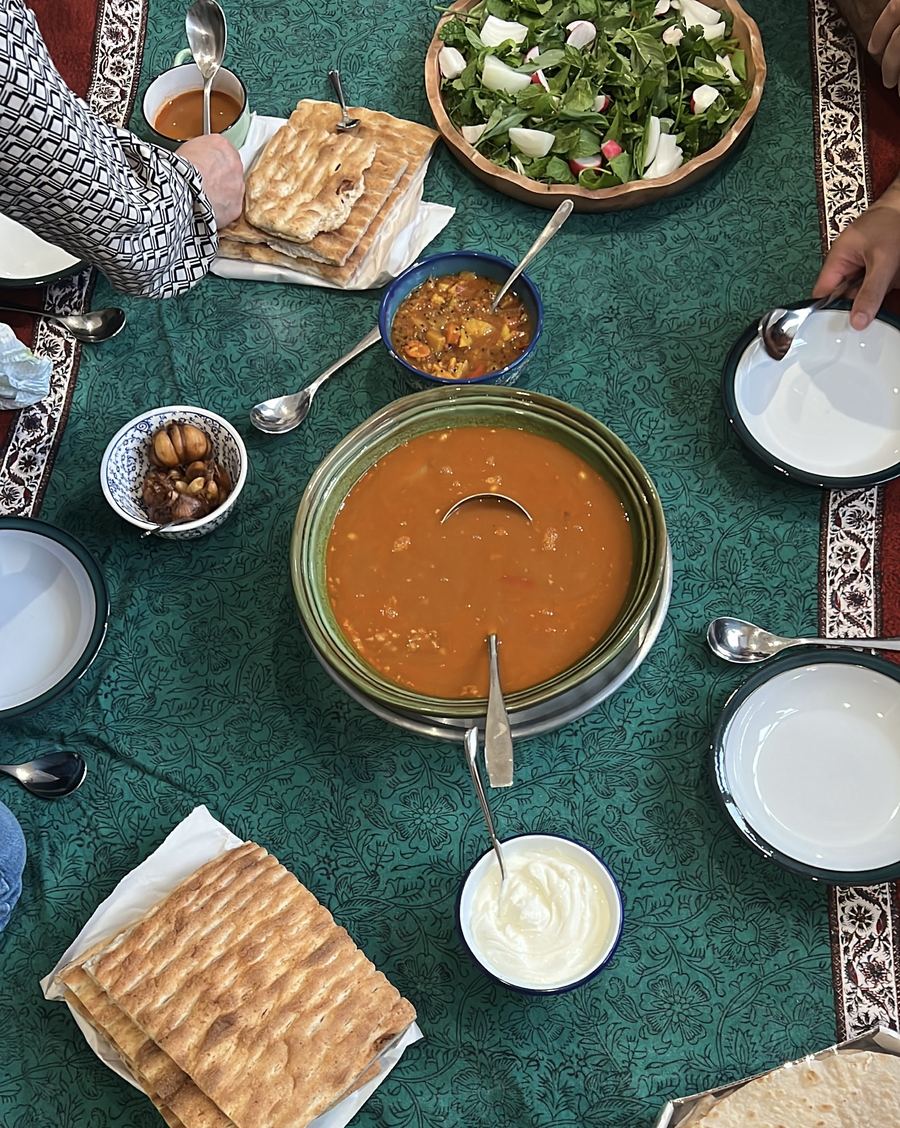 A green sofreh cloth set with ash soup, fresh herbs, warm bread and yoghurt.