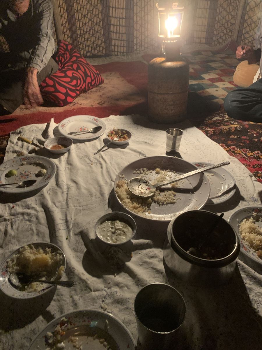 An evening meal on a takht, lit by lantern light, plates shared across the cloth.